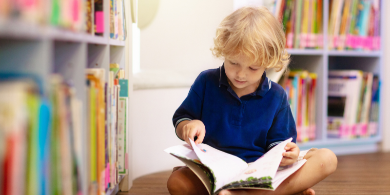 Young boy reading book in library.